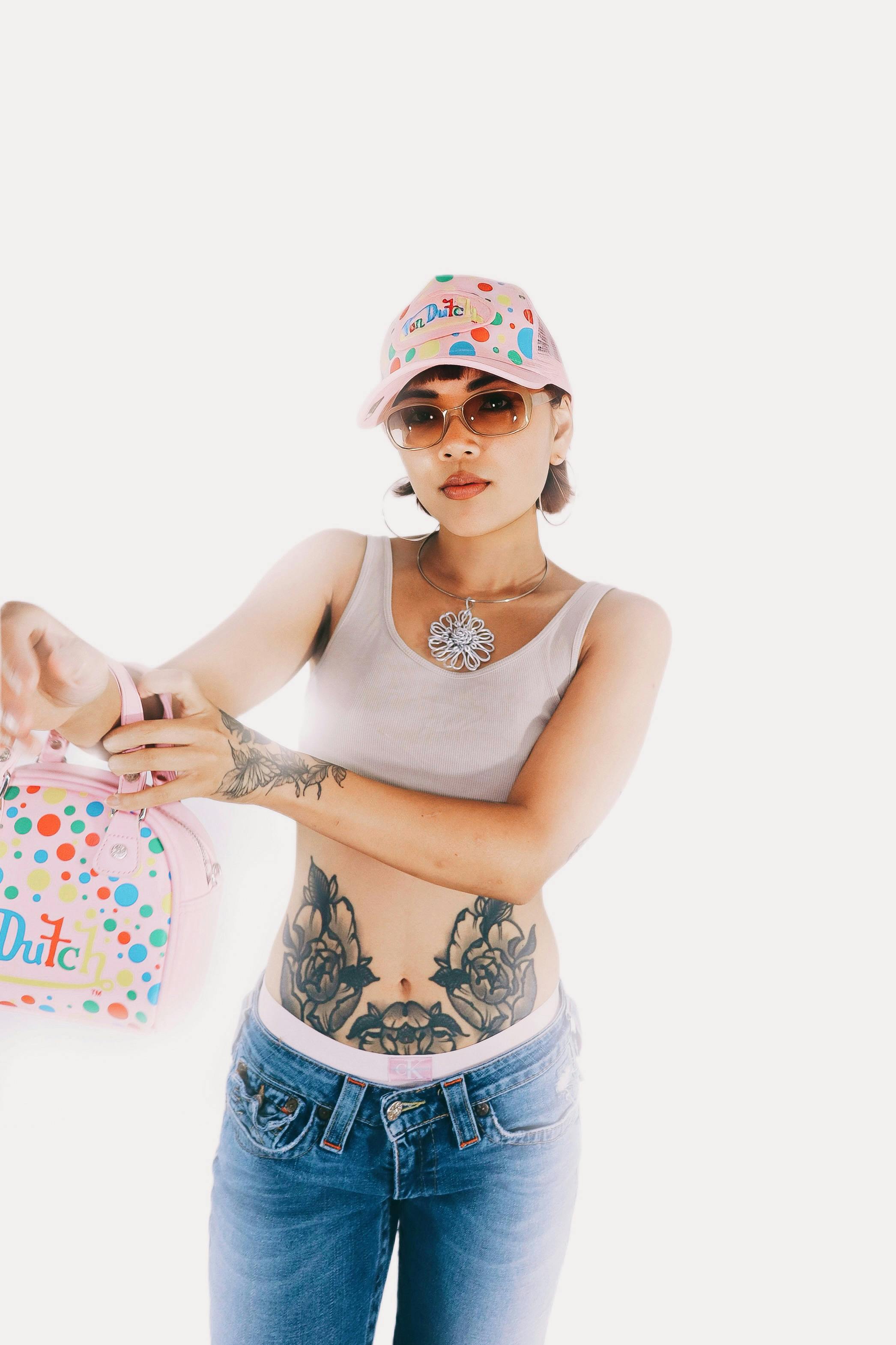 Stylish portrait of a tattooed woman in casual attire, showcasing modern fashion accessories on a white background.