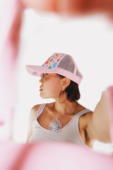 Stylish young woman wearing a cap and necklace taking a selfie. Bright and modern portrait.