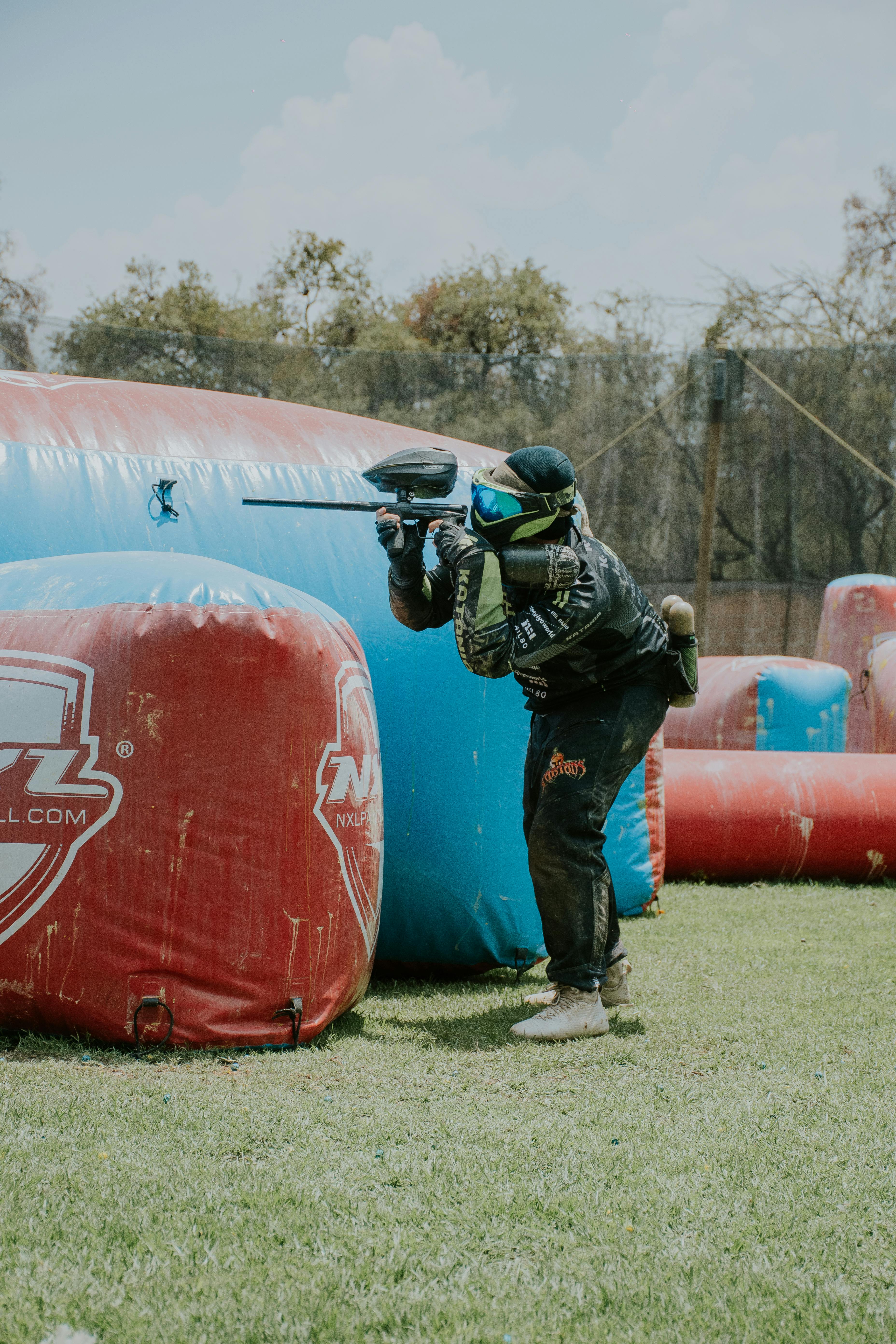 Le joueur vise lors d'un jeu de paintball en plein air avec des barrières colorées. Prescription Goggle Inserts - Player takes aim during outdoor paintball game with colorful barriers.