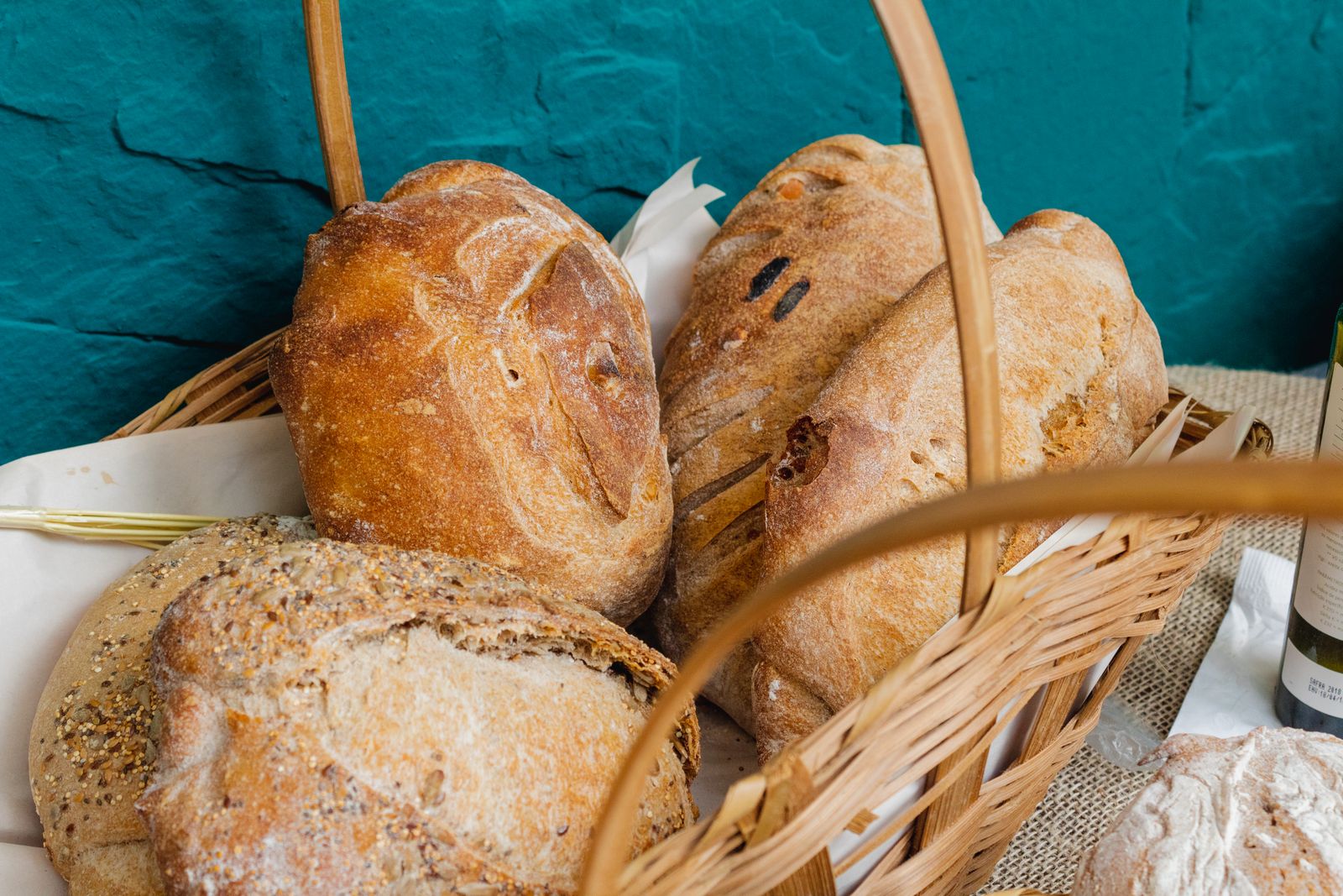 Crusty rustic loaves piled in a wicker basket against a teal wall