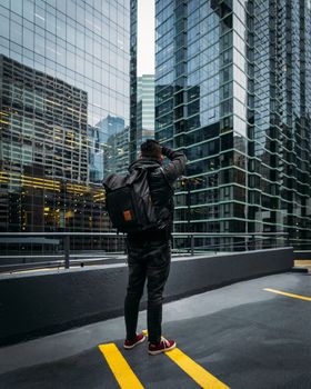 在现代城市环境中，一名背着背包的男子正在拍摄高耸的摩天大楼