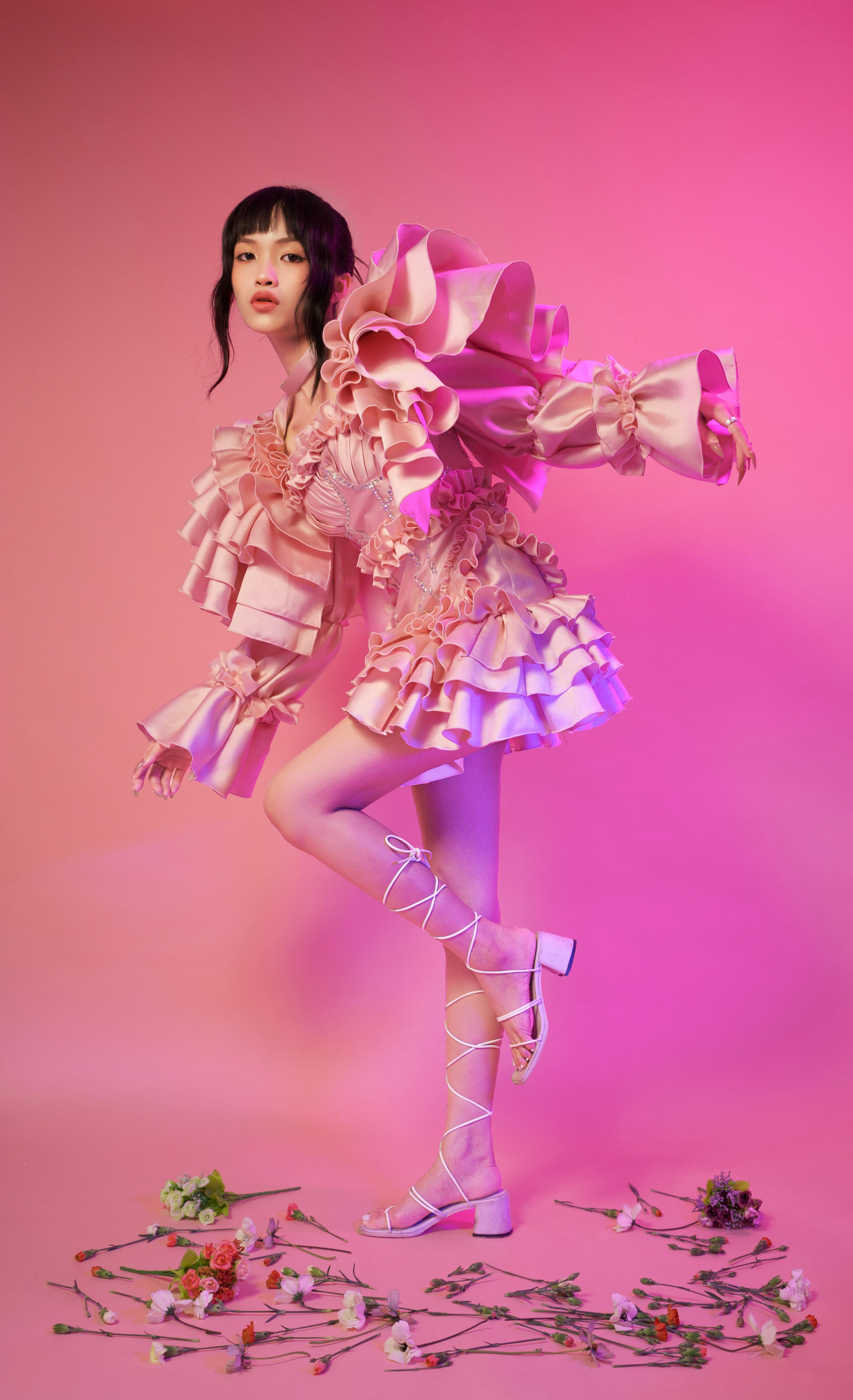 Woman in a pink ruffled dress posing elegantly in a studio with scattered flowers.