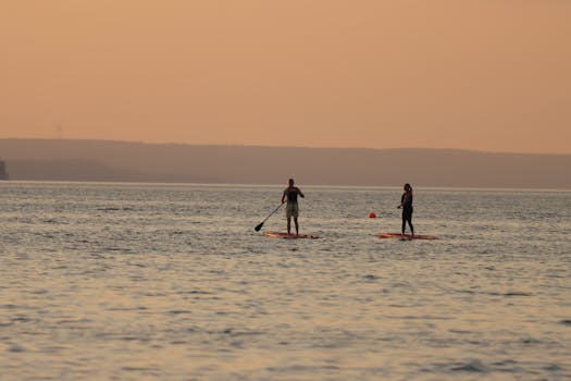 Two people paddleboarding at sunset on Lake Vättern, Jönköping, Sweden.