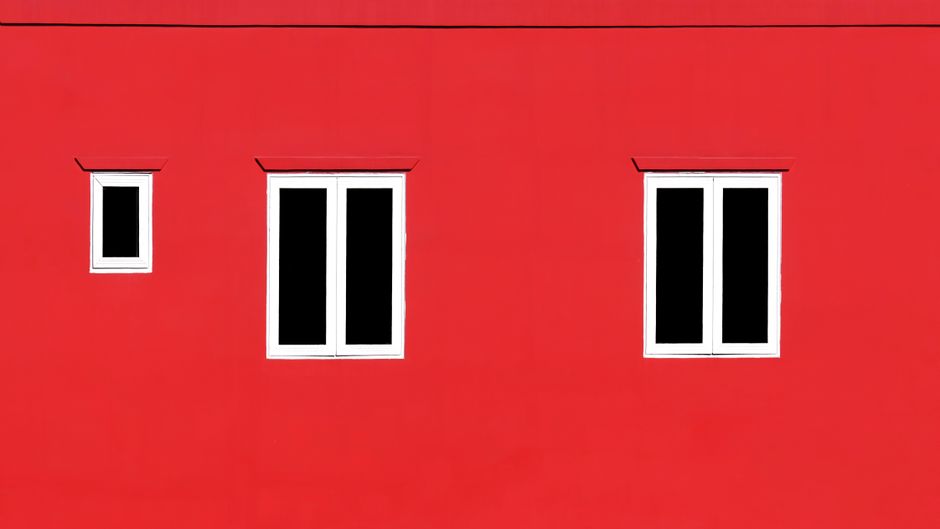 Close-up of a vibrant red wall featuring minimalist white windows.