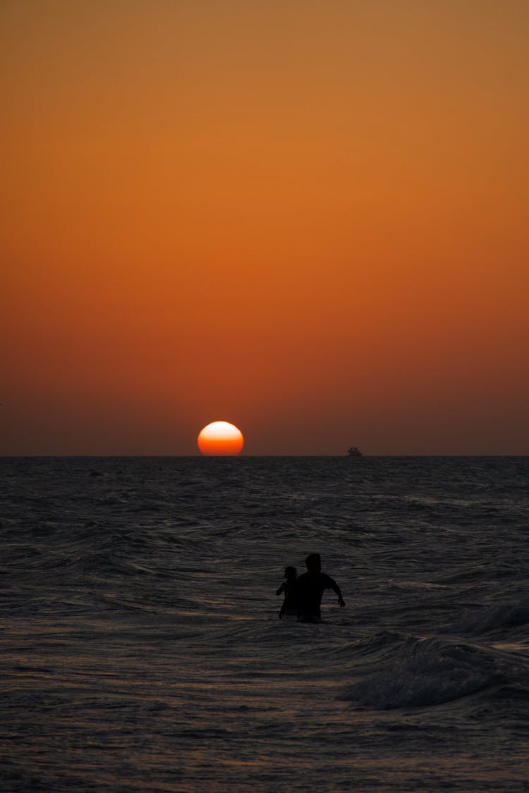 People Silhouette In Sea At Sunset