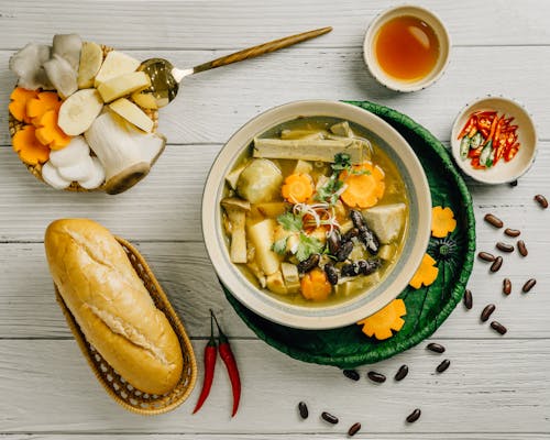 A bowl of soup with bread and vegetables on a white table