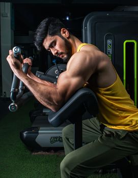 Muscular man in a gym performing bicep curls on a machine, showcasing strength and dedication.