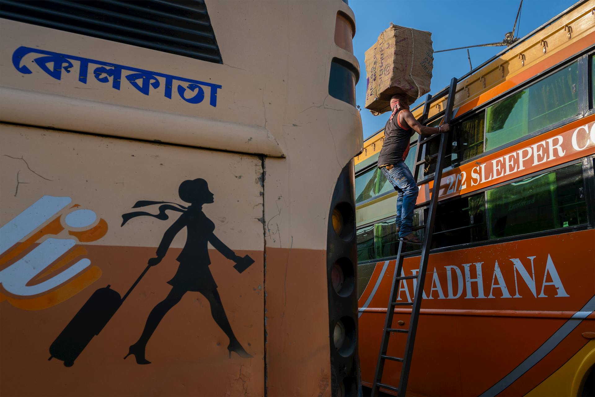 Man with Pacakge on Head Standing on Ladder by Buses