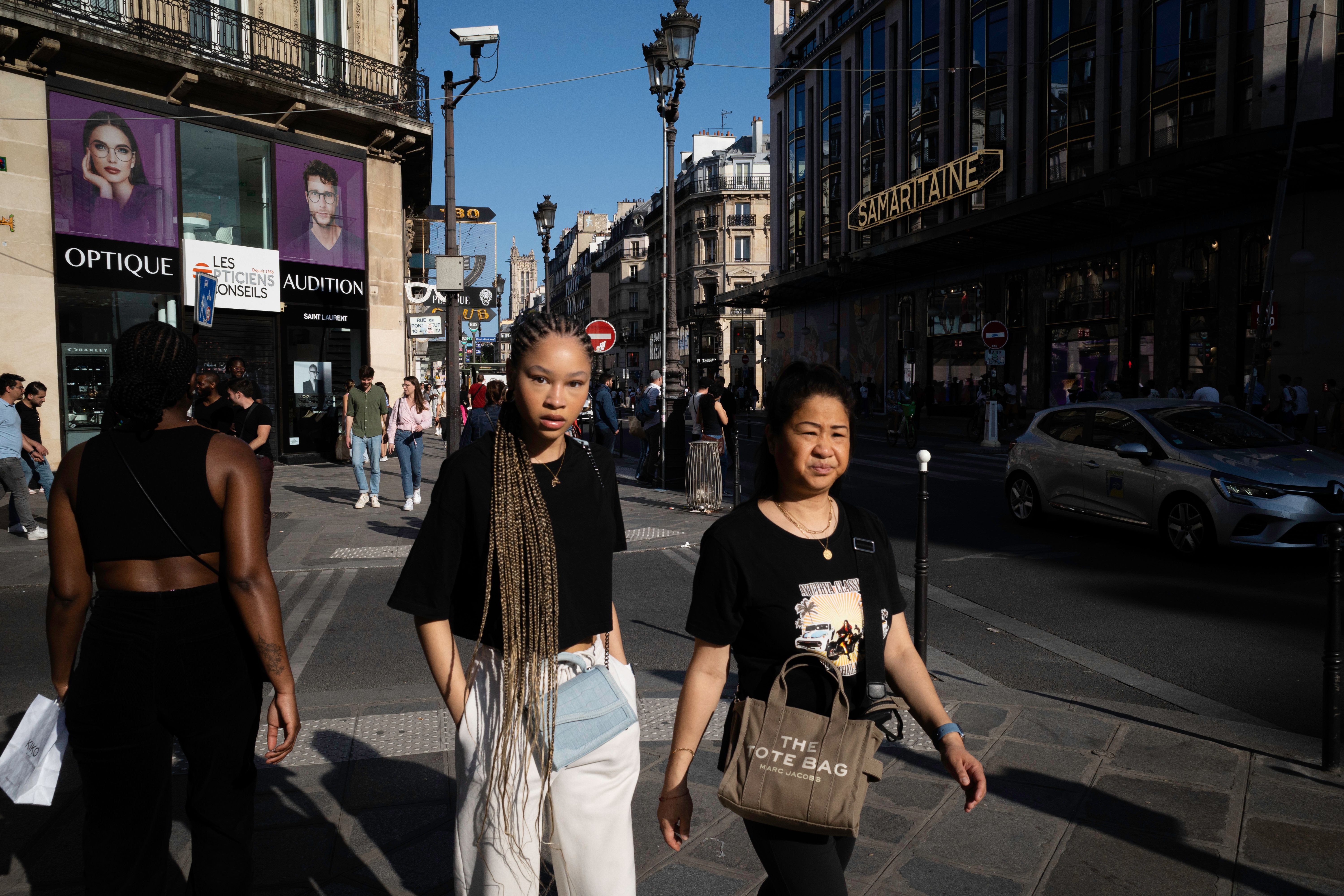 People walking in sunlight around the iconic Samaritaine building in Paris.