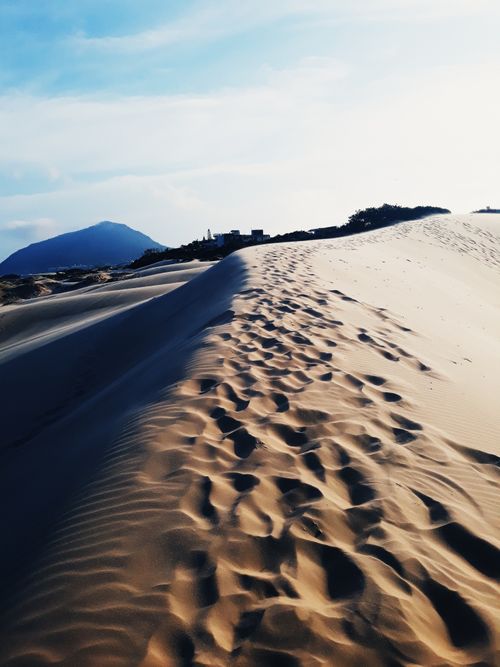 Free Tranquil desert dunes with footprints, bathed in warm sunset light, capturing nature's serene beauty. Stock Photo