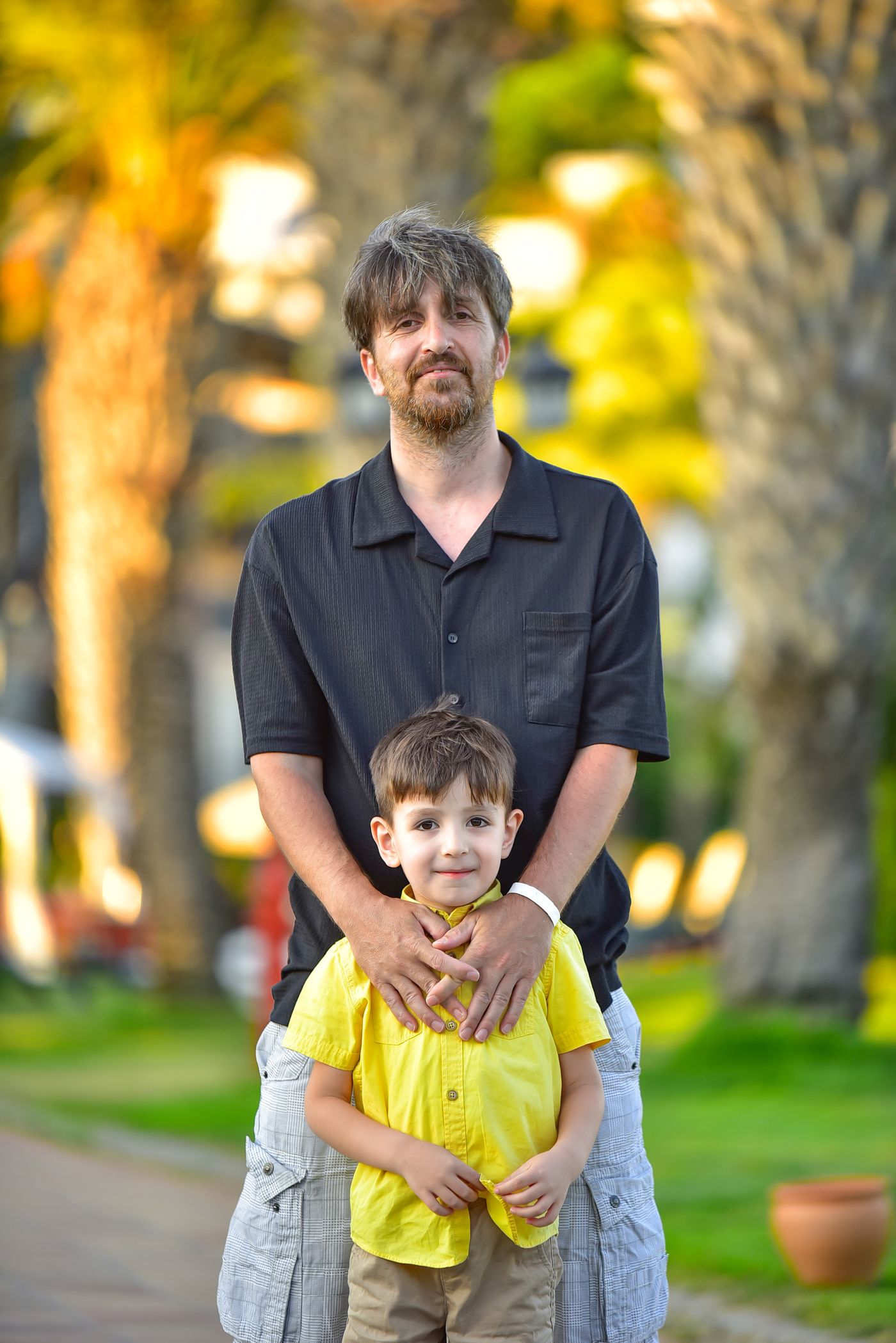 A father and his young son standing together in a park
