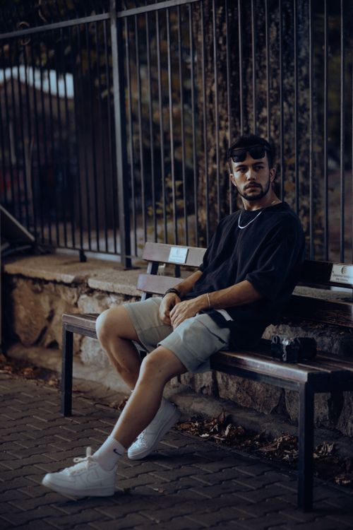 Free Casual young man sitting on a bench in urban setting at twilight, showcasing street fashion. Stock Photo