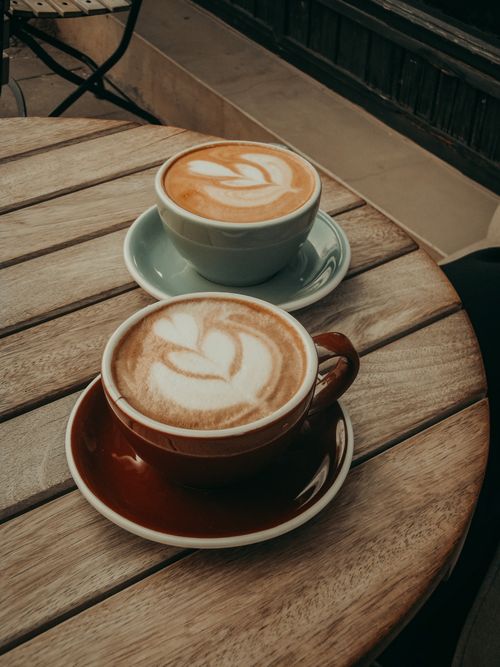 Free High-angle view of two cappuccinos with latte art on a rustic wooden table in a café. Stock Photo