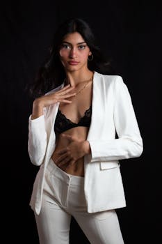 Stylish woman in a white suit posing against a black background, exuding elegance and confidence.