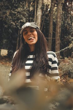 一位年轻女子面带微笑，穿着条纹衬衫，戴着帽子，在树林里享受美好的一天