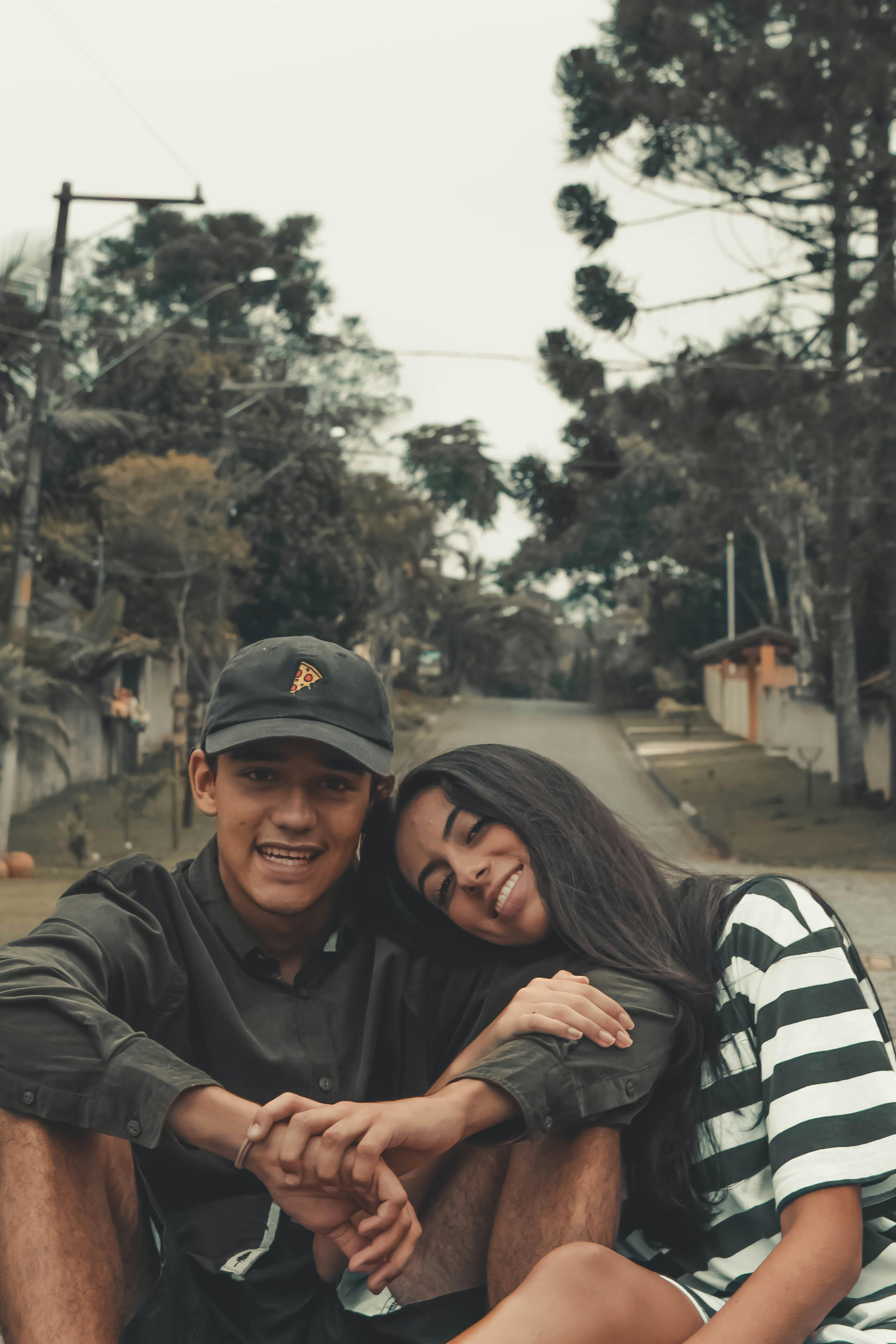 Two young adults sitting on a quiet street smiling and enjoying a moment together.