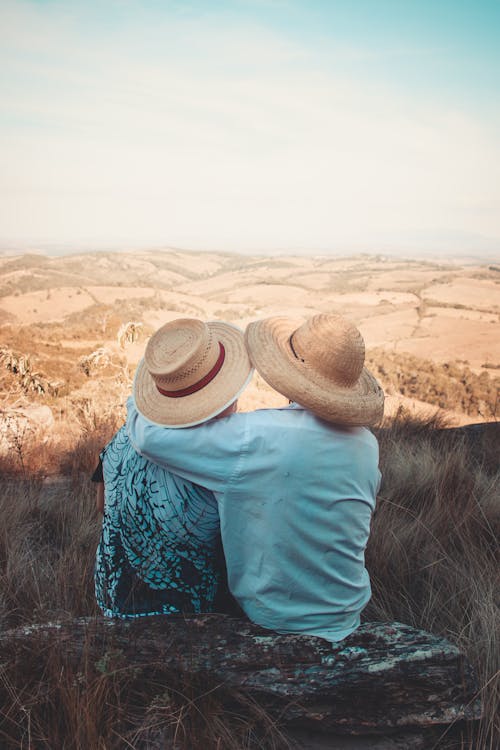 Free Two Person Wearing Sunhats Sitting on Rock Stock Photo