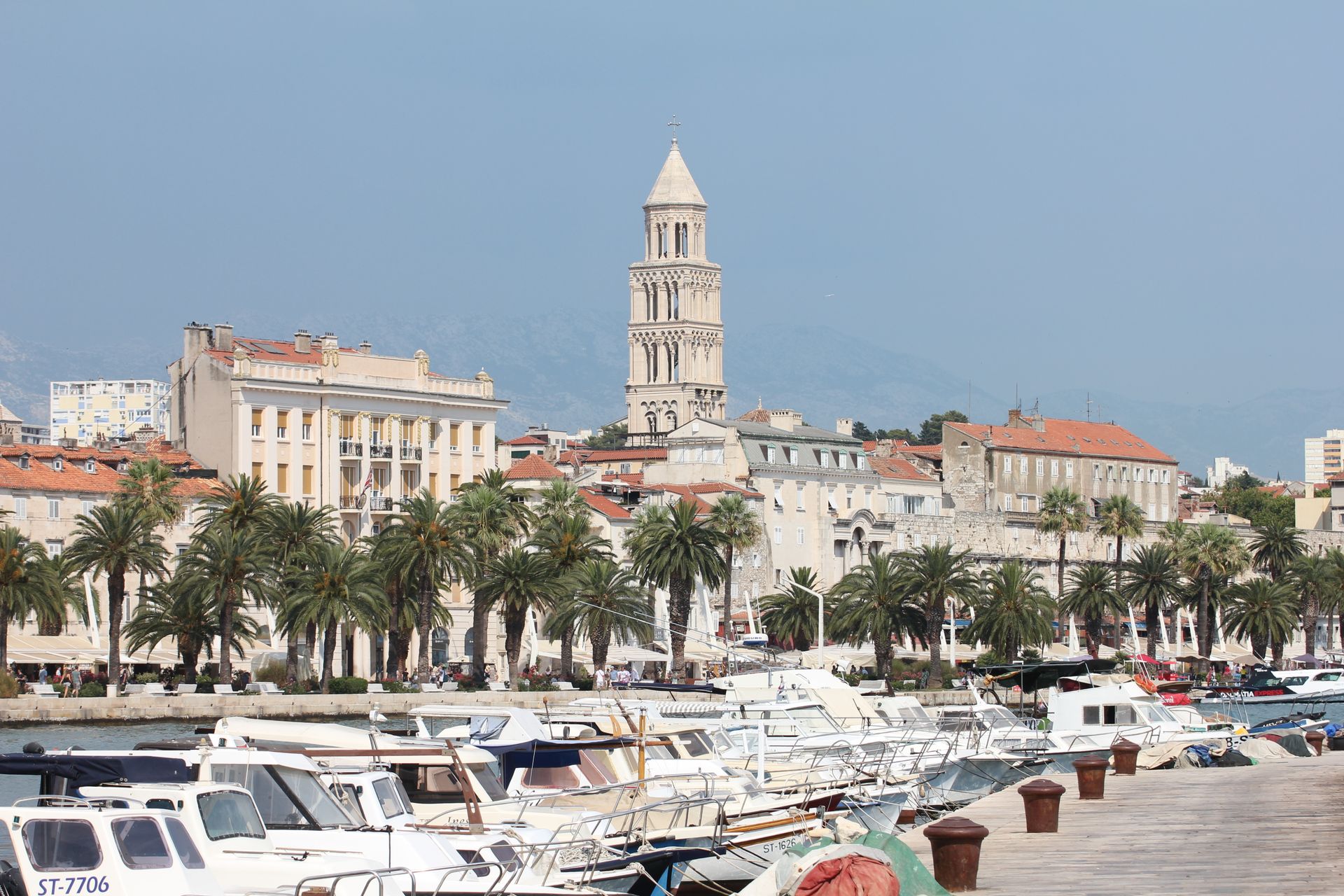 Sunlit view of Split marina with palm trees, boats, and historic buildings in Croatia.