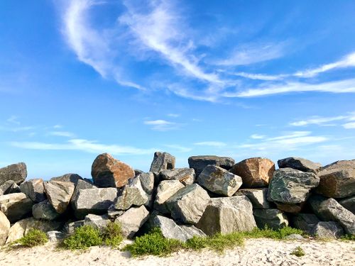Free Pile of sunlit rocks against a clear blue sky with white clouds. Stock Photo