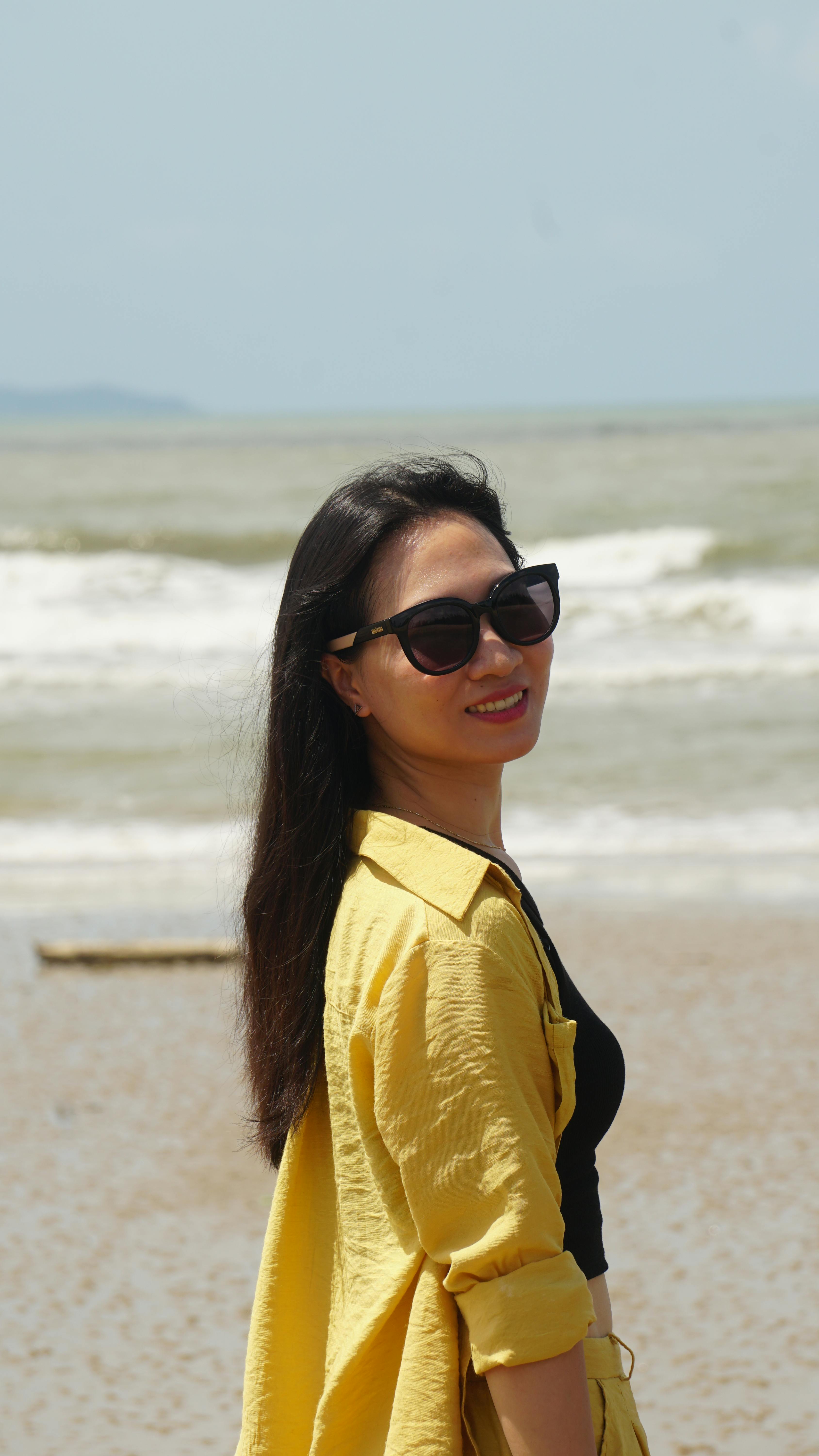 Woman smiling by the beach in a yellow blouse and sunglasses, Móng Cái, Vietnam.