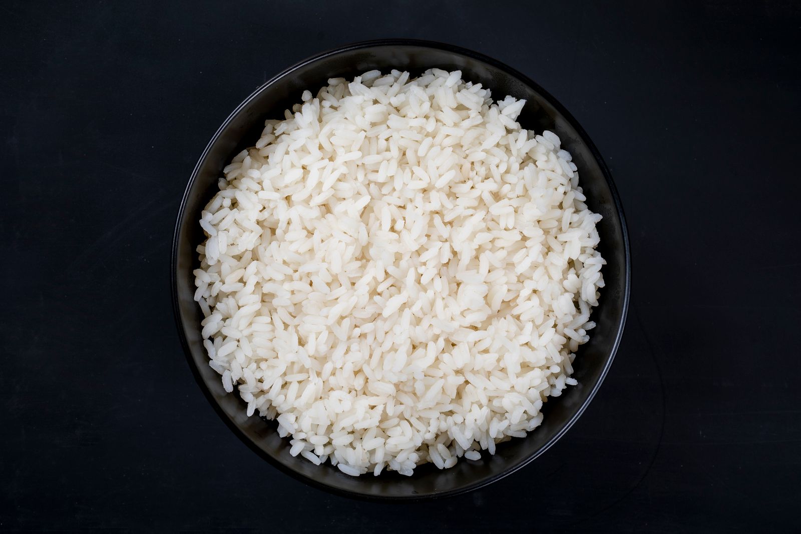Bowl of freshly cooked white rice against a dark background.