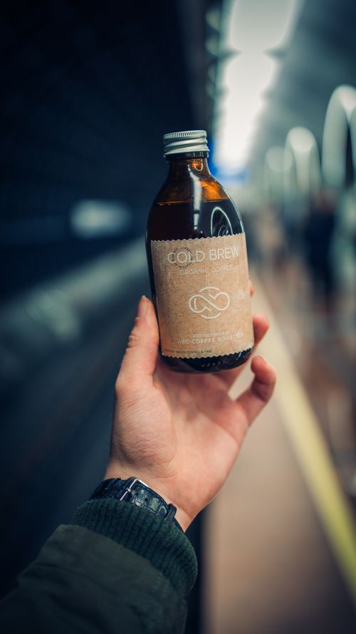 Free Close-up of a hand holding a labeled cold brew coffee bottle in a metro station. Stock Photo