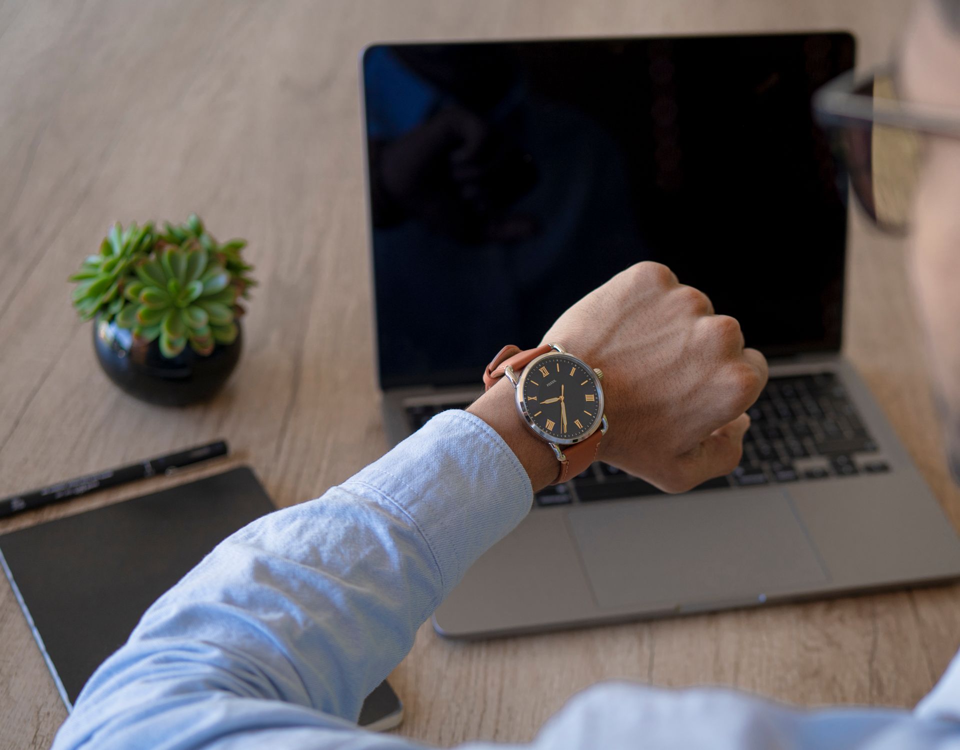 Adult male checks time on watch while working on a laptop at home office.