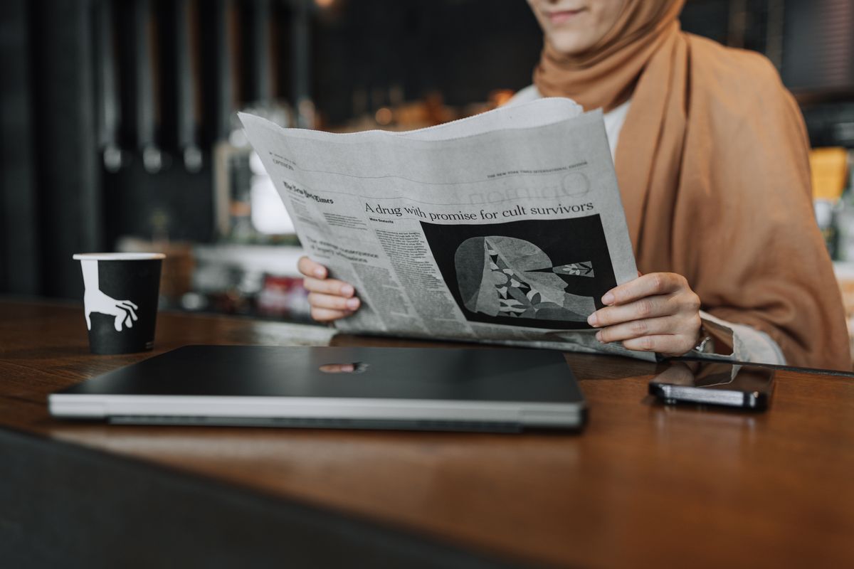 نماذج وأدوات عربية أخرى في السوق امرأة ترتدي الحجاب تقرأ صحيفة في مقهى بجانب حاسوبها
