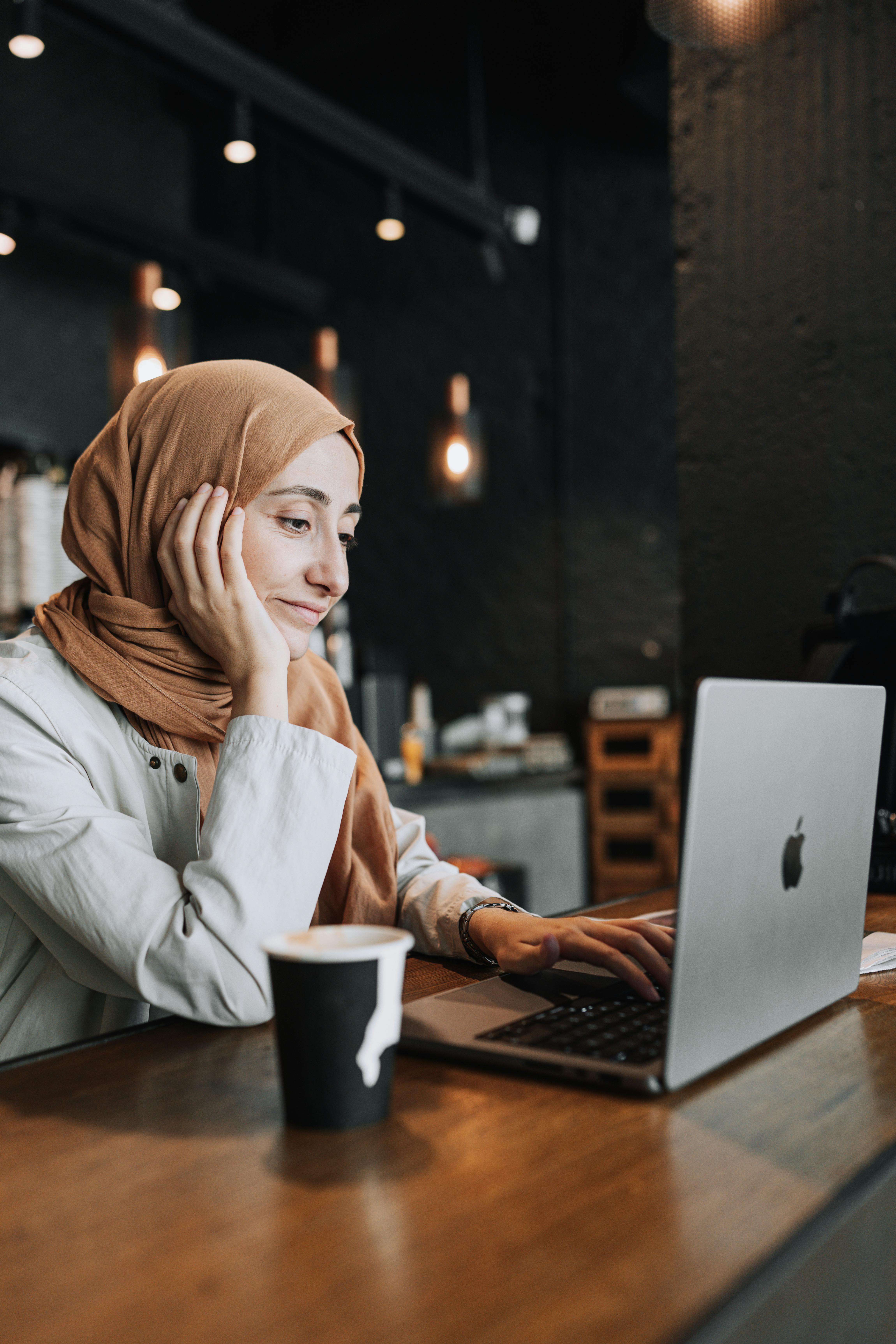 woman in headscarf working on laptop at cafe