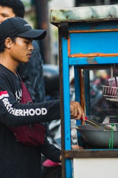 Asian man cooking at a street food stand, focused on his task. Urban setting.