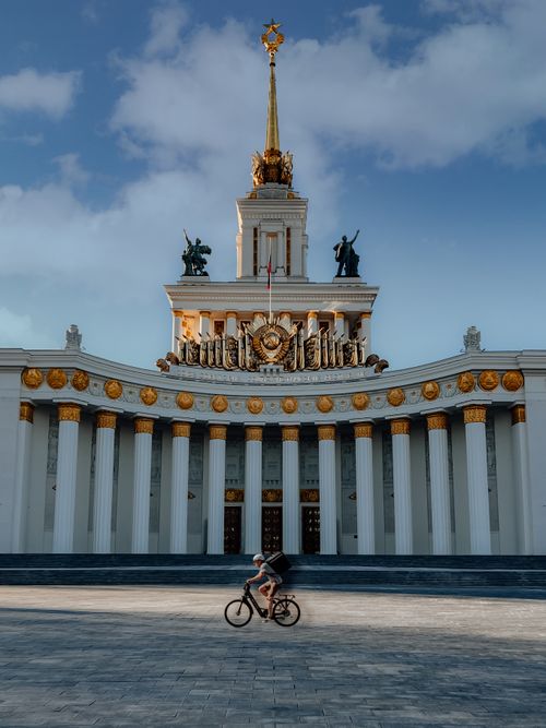 Free A cyclist rides past the iconic architectural facade of the Moscow Exhibition Center under a blue sky. Stock Photo
