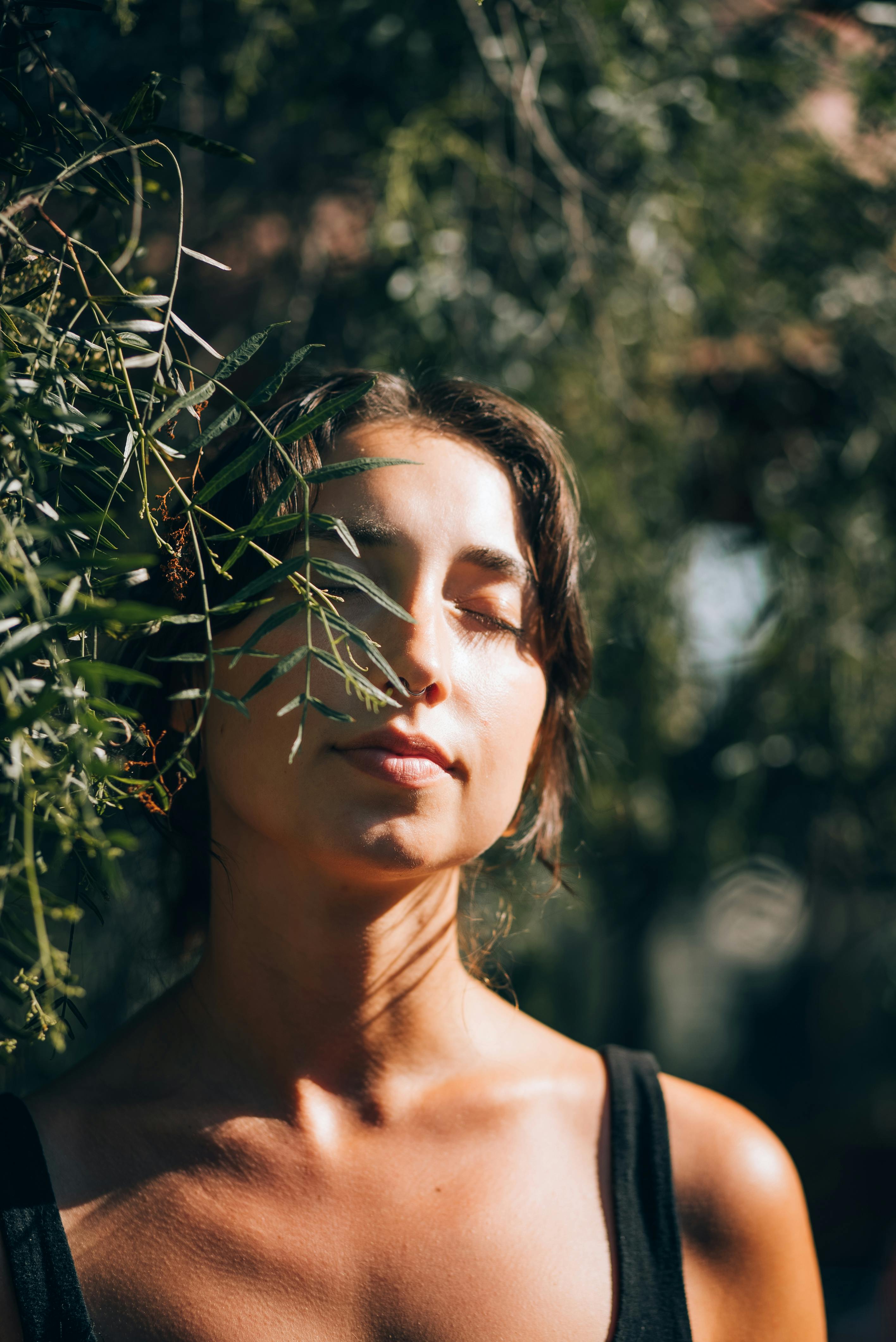 A tranquil portrait of a woman meditating outdoors with eyes closed, surrounded by greenery.