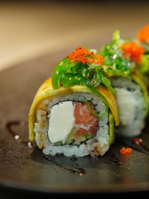 Free Delicious sushi roll with cream cheese, seaweed, and fish roe on a dark plate. Perfect for Japanese cuisine enthusiasts. Stock Photo