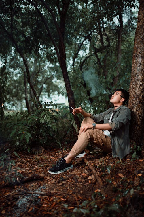 A man sitting in the woods with a cigarette