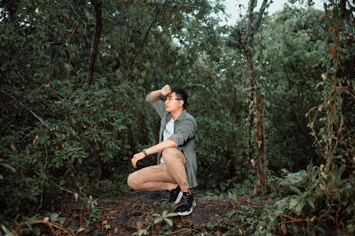 A man crouching in the woods with his hands on his knees