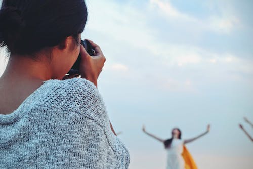 Woman Taking Picture of Woman Dancing Under White Sky