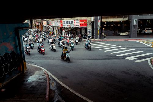 Free Bustling scooter traffic under a bridge at a city crosswalk, showcasing urban life. Stock Photo