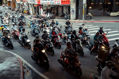 Free A bustling urban intersection filled with scooters and diverse riders in a city street scene. Stock Photo