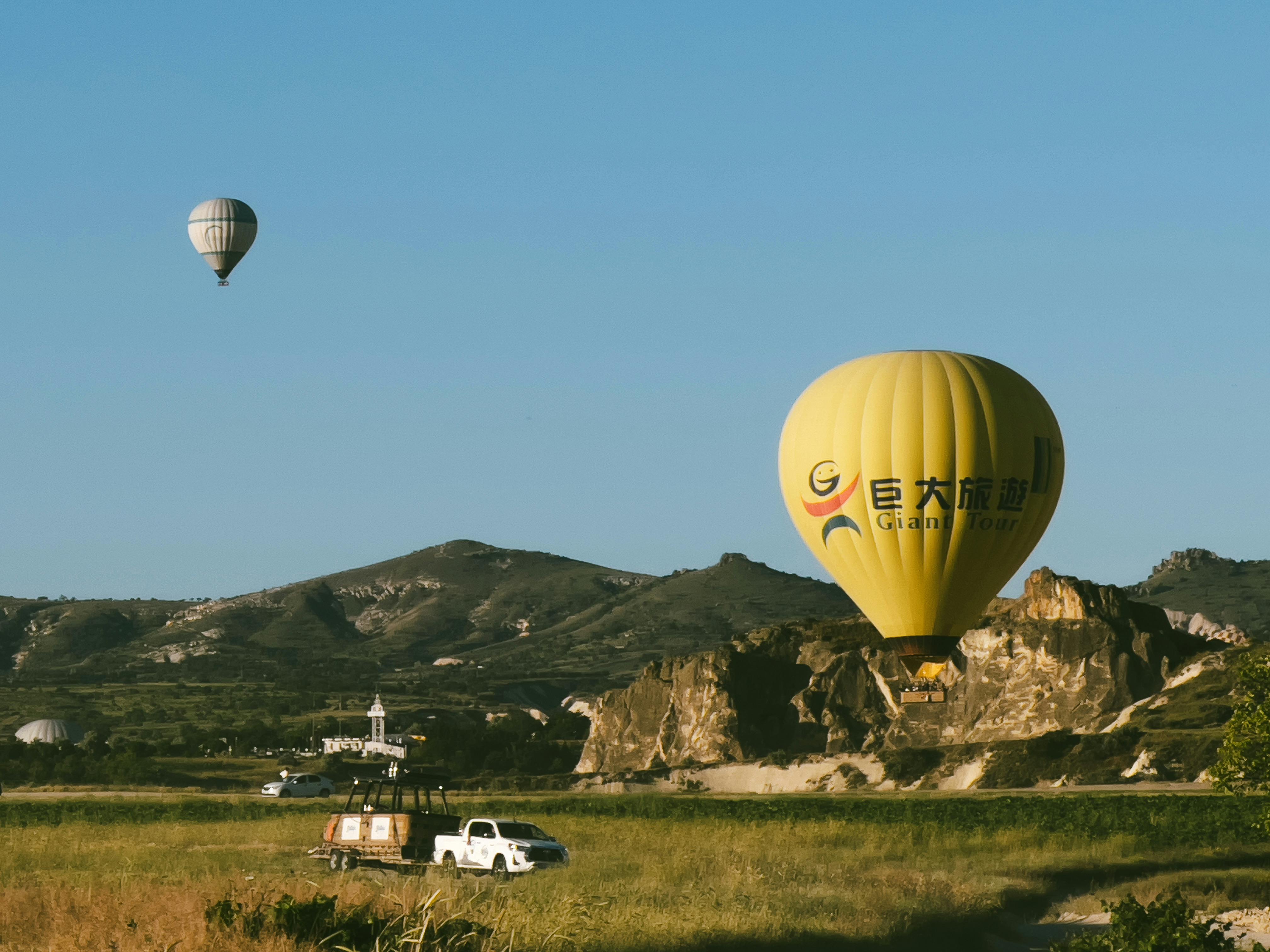 Hot air balloons drifting over rocky landscapes in Cappadocia during a clear summer day.