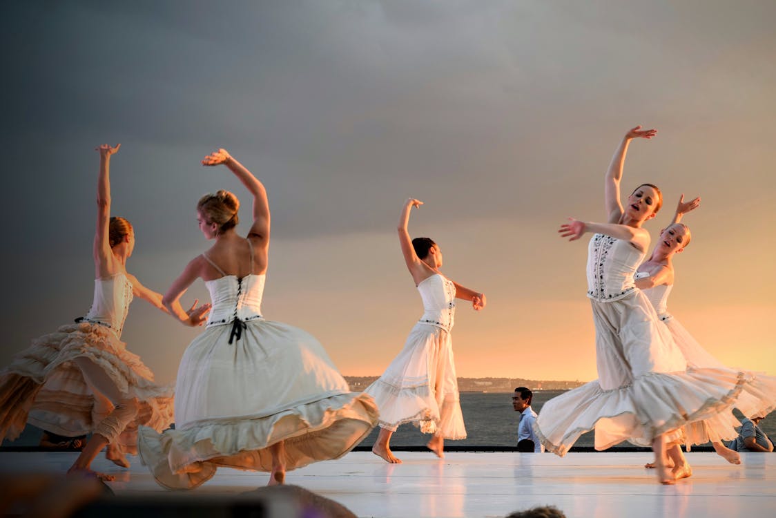 5名穿著白色連衣裙的婦女在日落時分在灰色的天空下跳舞