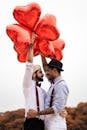 Two Men  Embracing while Holding Heart Balloons