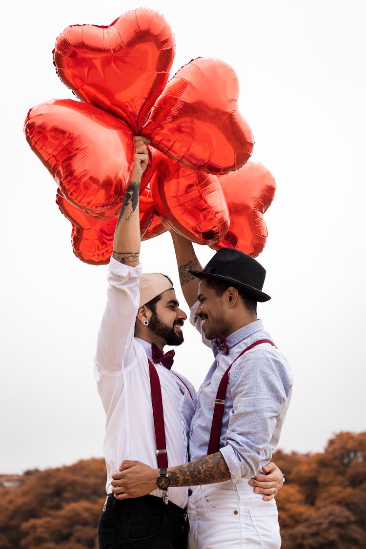 Two Men  Embracing While Holding Heart Balloons