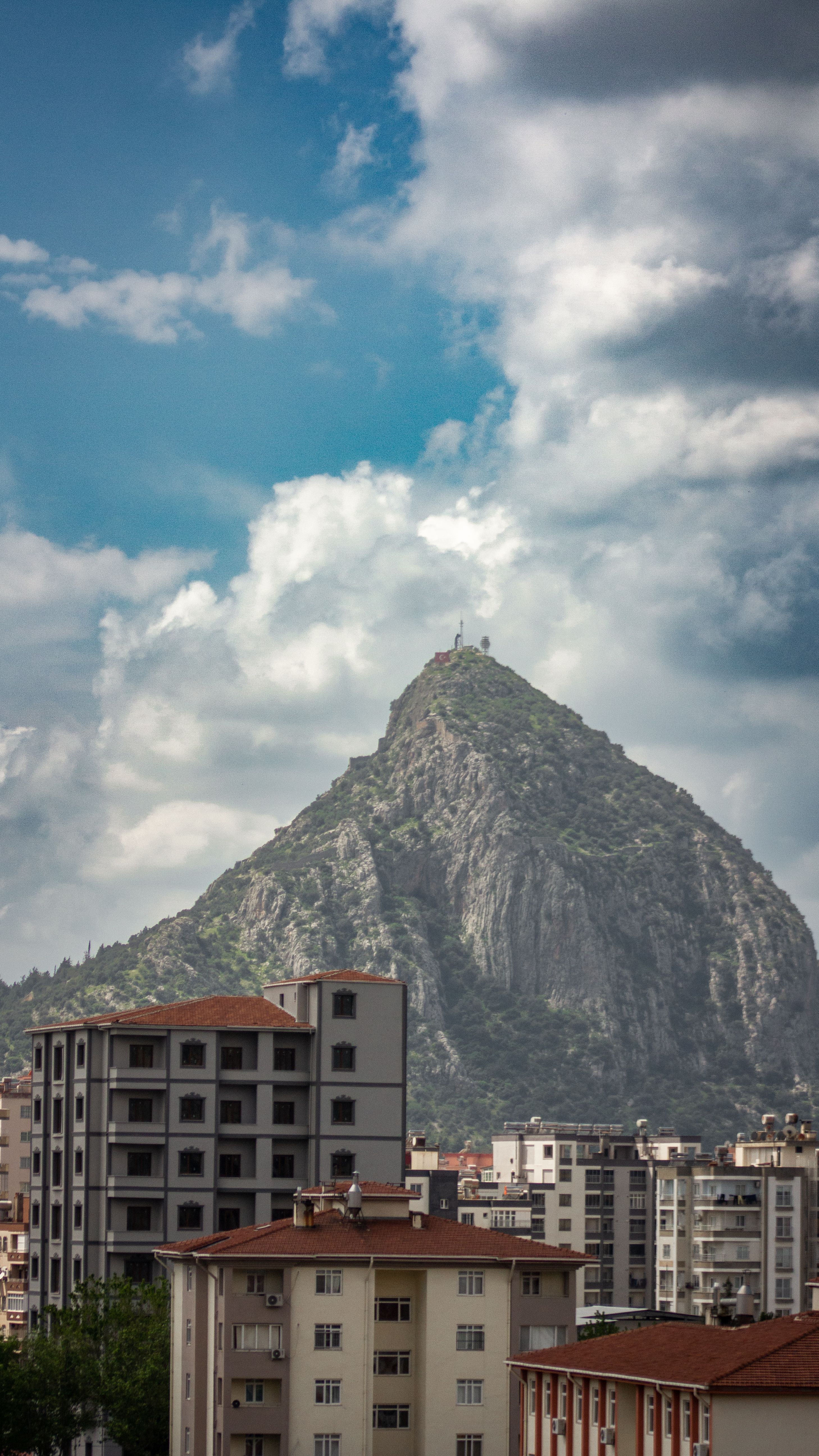 City skyline with apartment buildings and a towering mountain under a cloudy sky.