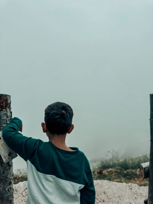 Free Boy wearing sweatshirt looks into a misty, foggy landscape creating a serene, contemplative scene. Stock Photo