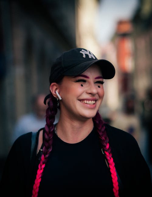 Portrait of a Young Woman with Pink Braids and a Cap Walking on a Street and Smiling 