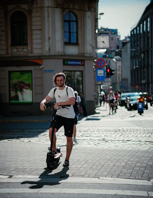 Free A young man navigates city streets on an electric scooter, showcasing modern urban commuting. Stock Photo