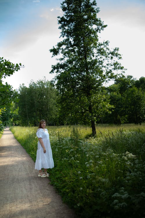 Bride in Wedding Dress Posing on Dirt Road Near Meadow