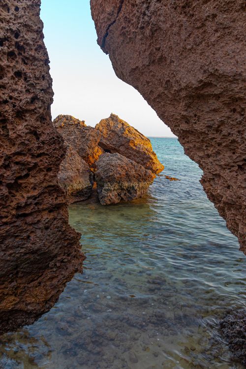 Free Captivating view of eroded rocks and clear sea through a coastal crevice at sunset. Stock Photo