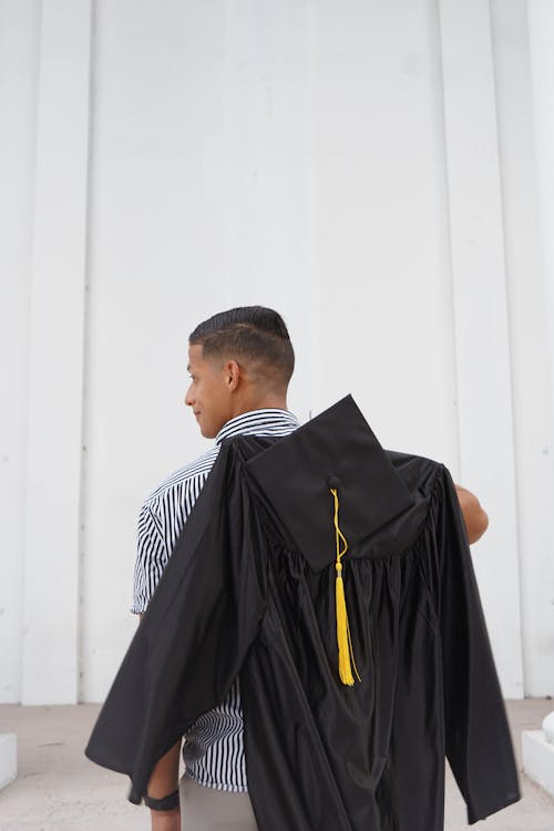 Back View of a Man Holding a Graduation Gown and a Mortarboard 