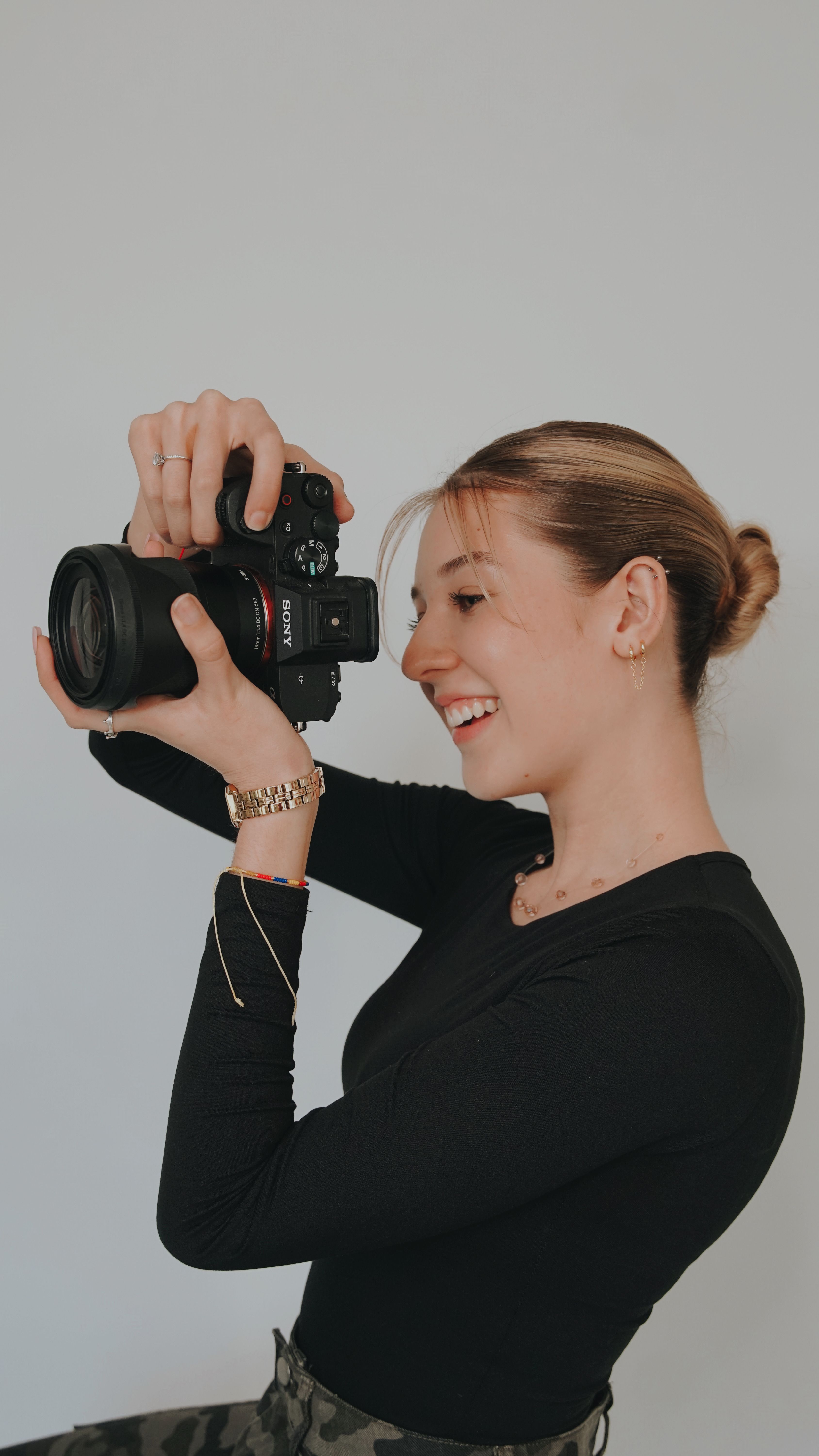 Happy young woman holding a camera, smiling against a white background in Miami, Florida.